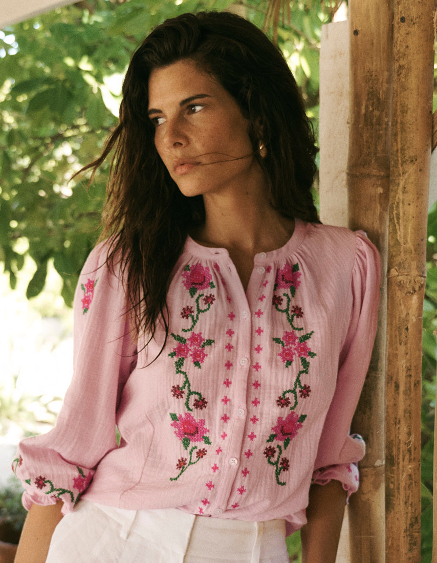 Eine Frau in einer rosa bestickten Bluse steht im Freien vor einem grünen Hintergrund